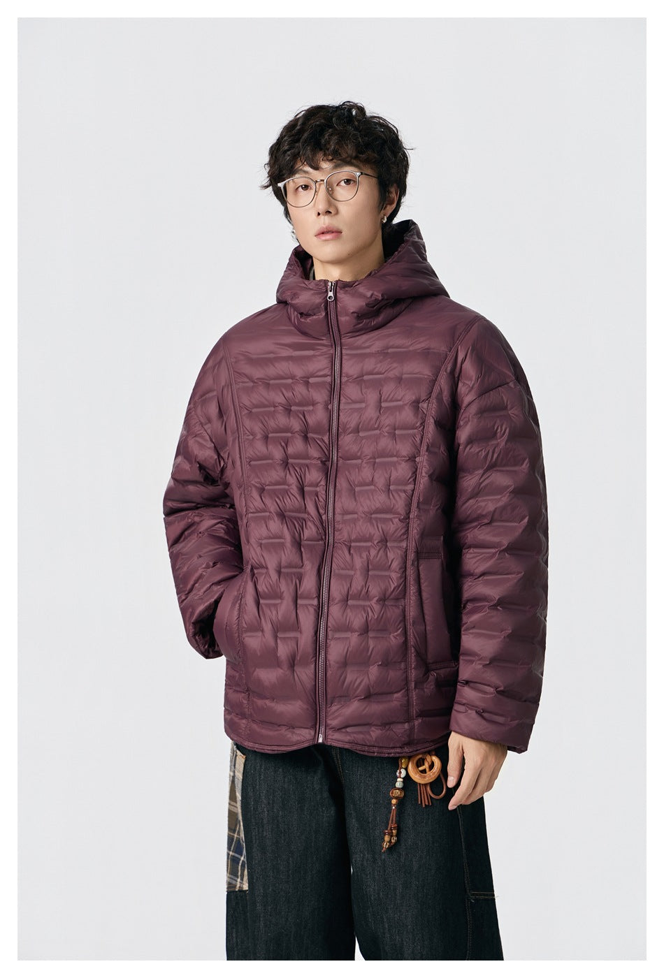 Model wearing a burgundy hooded quilted puffer jacket zipped, with dark jeans, three-quarter view