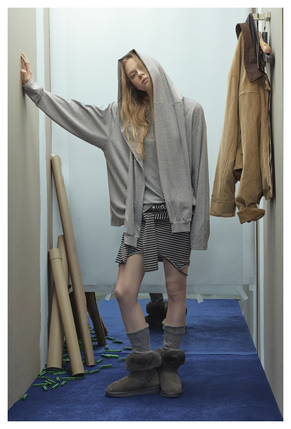 Model wearing a gray hooded layer over a gray top and black-and-gray striped skirt, shown from the front.
