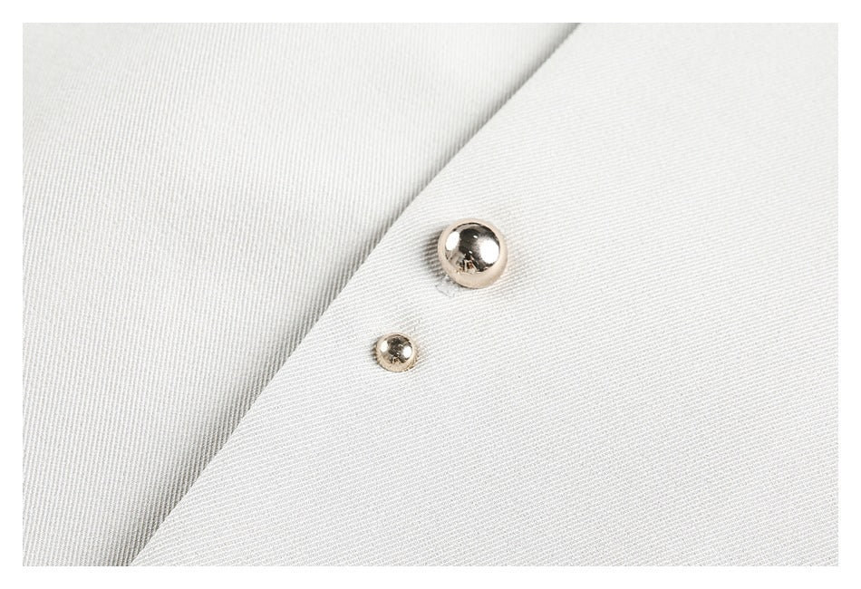 Close-up of two shiny metal snaps on a light ivory garment panel.