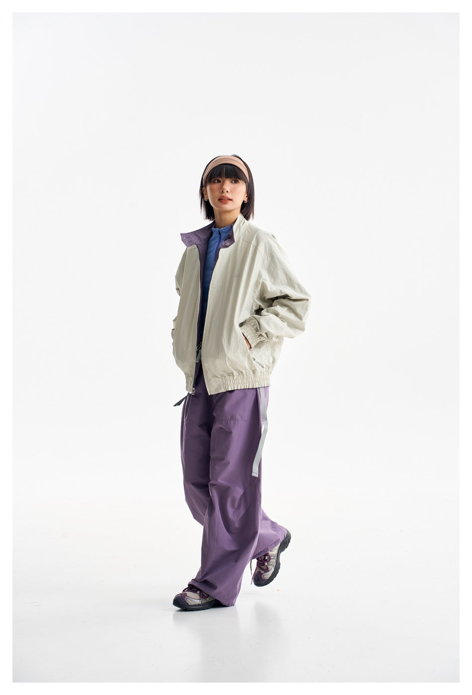 Model wearing a light gray zip jacket with a purple collar and loose purple pants, shown from the front.