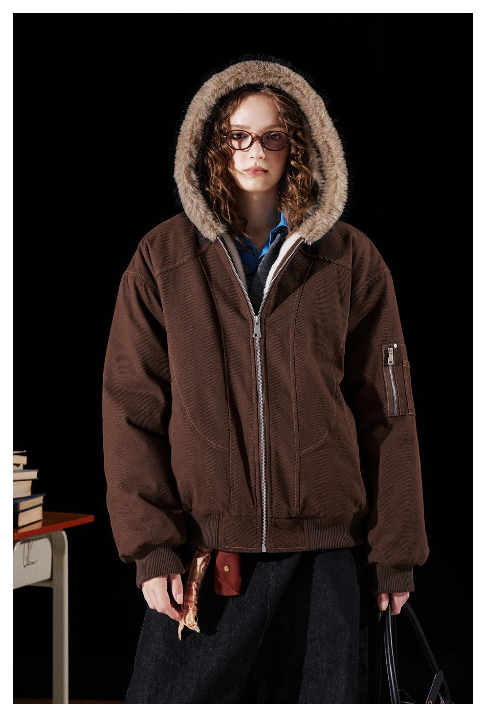 Model wearing a dark brown zip-front jacket with a tan fur-trimmed hood, ribbed cuffs and hem, and a sleeve pocket.