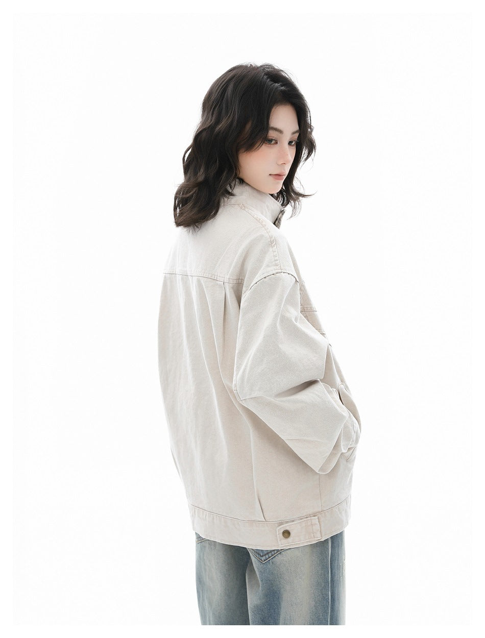 Angled back view of a model wearing a light beige jacket with a buttoned hem tab and blue jeans.