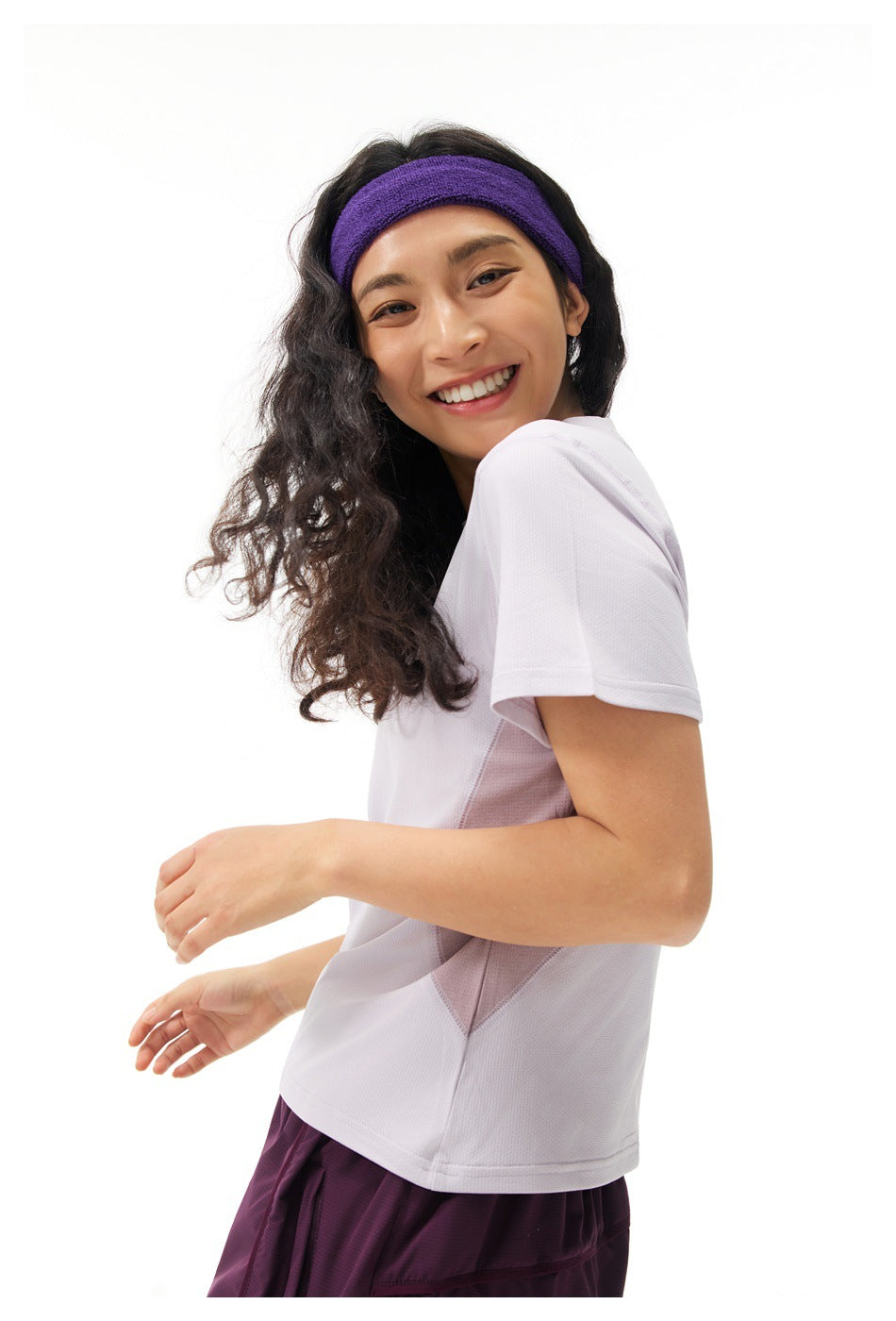 Model in a white short-sleeve top with pale mauve side panels and plum bottoms, wearing a purple headband.