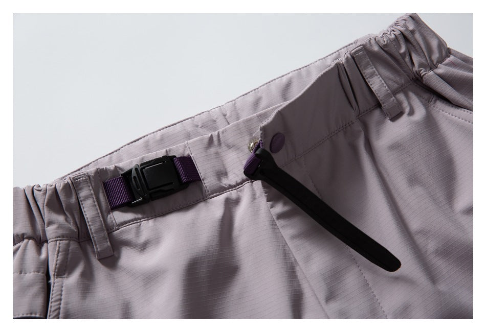 Close-up of mauve-gray pants showing an elastic waist, black buckle strap, button, and zipper pull.