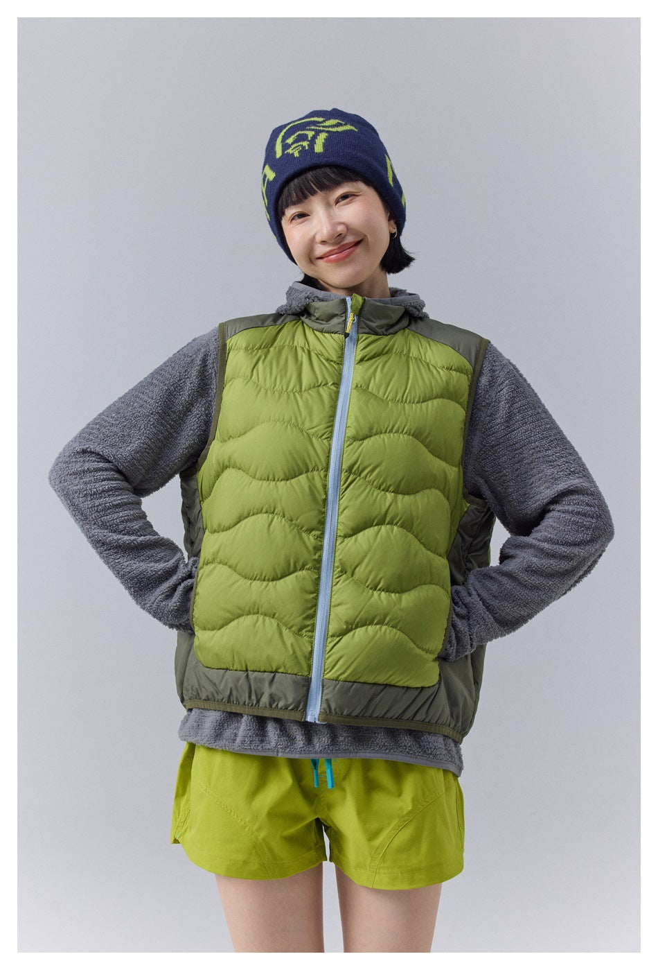 Front view of a model wearing a lime-green wave-quilted vest over a gray fleece.