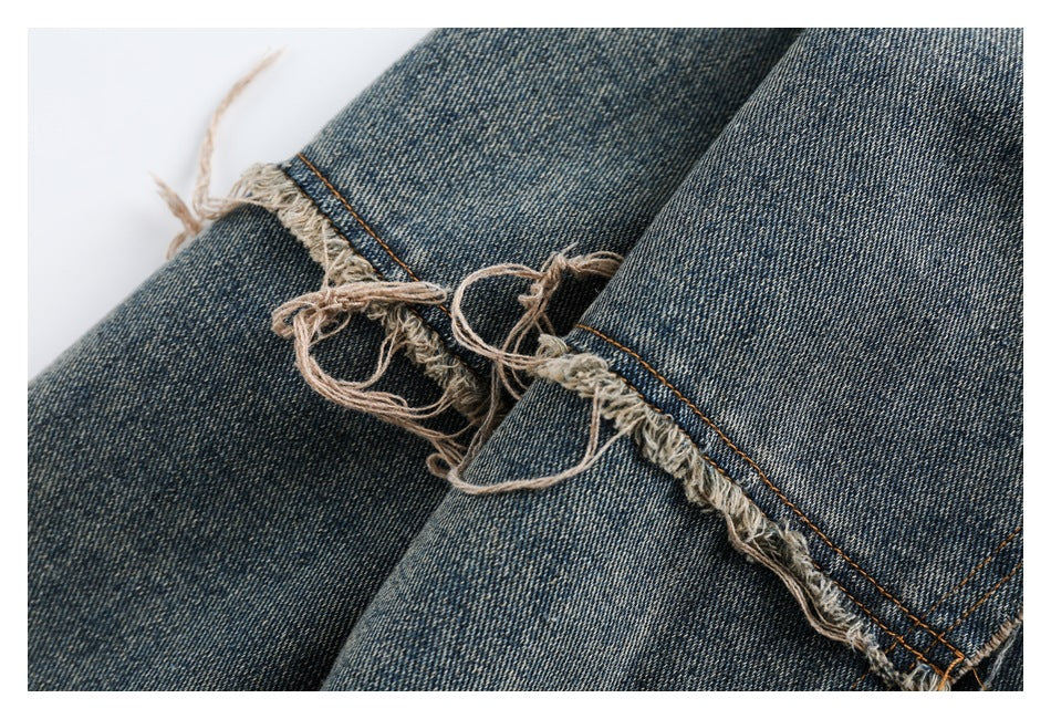 Close-up of distressed blue denim with a frayed opening and loose threads along an orange-stitched seam.