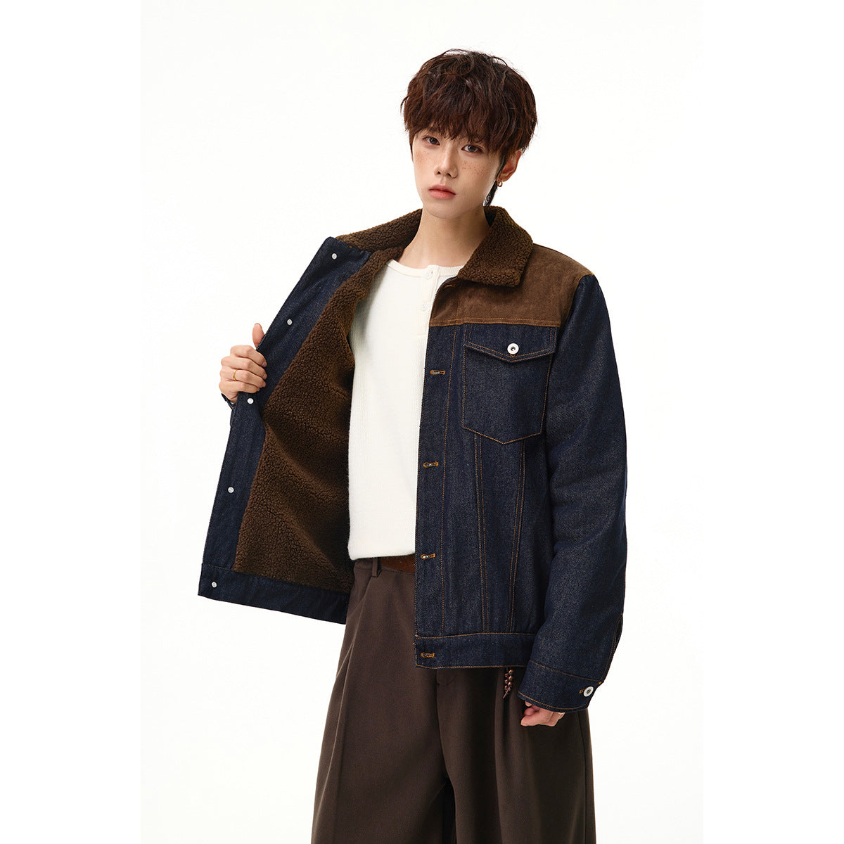 Model holds open a dark denim jacket to show its textured brown lining and sherpa collar.