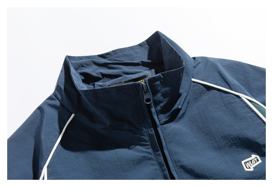 Close-up of a navy zip-up jacket with a high collar, white piping, and a small embroidered chest patch.