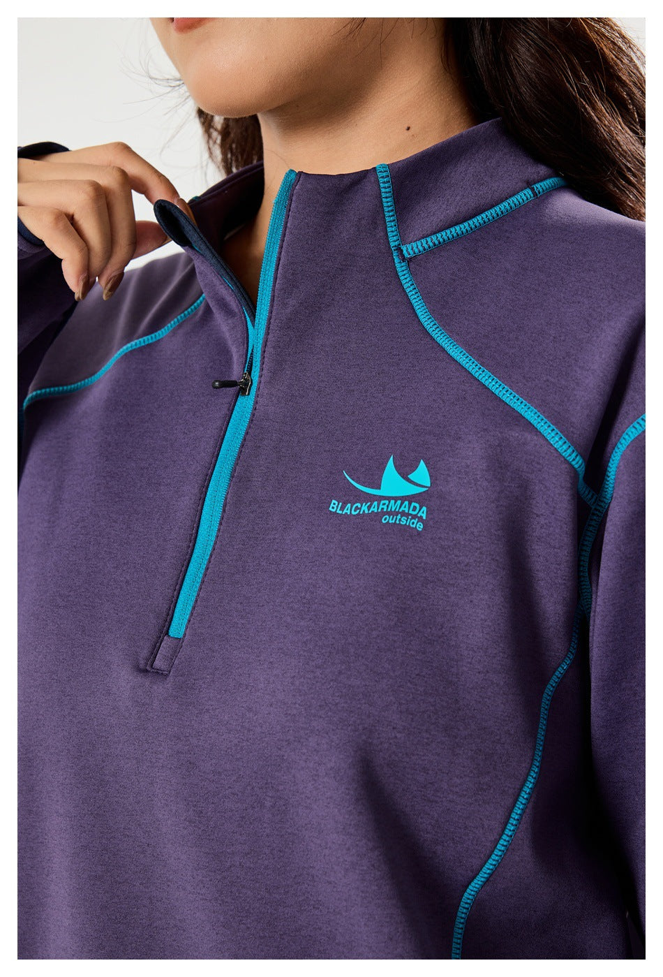 Close-up of a purple top showing its turquoise-trimmed quarter zip, high collar, stitching, and chest logo.