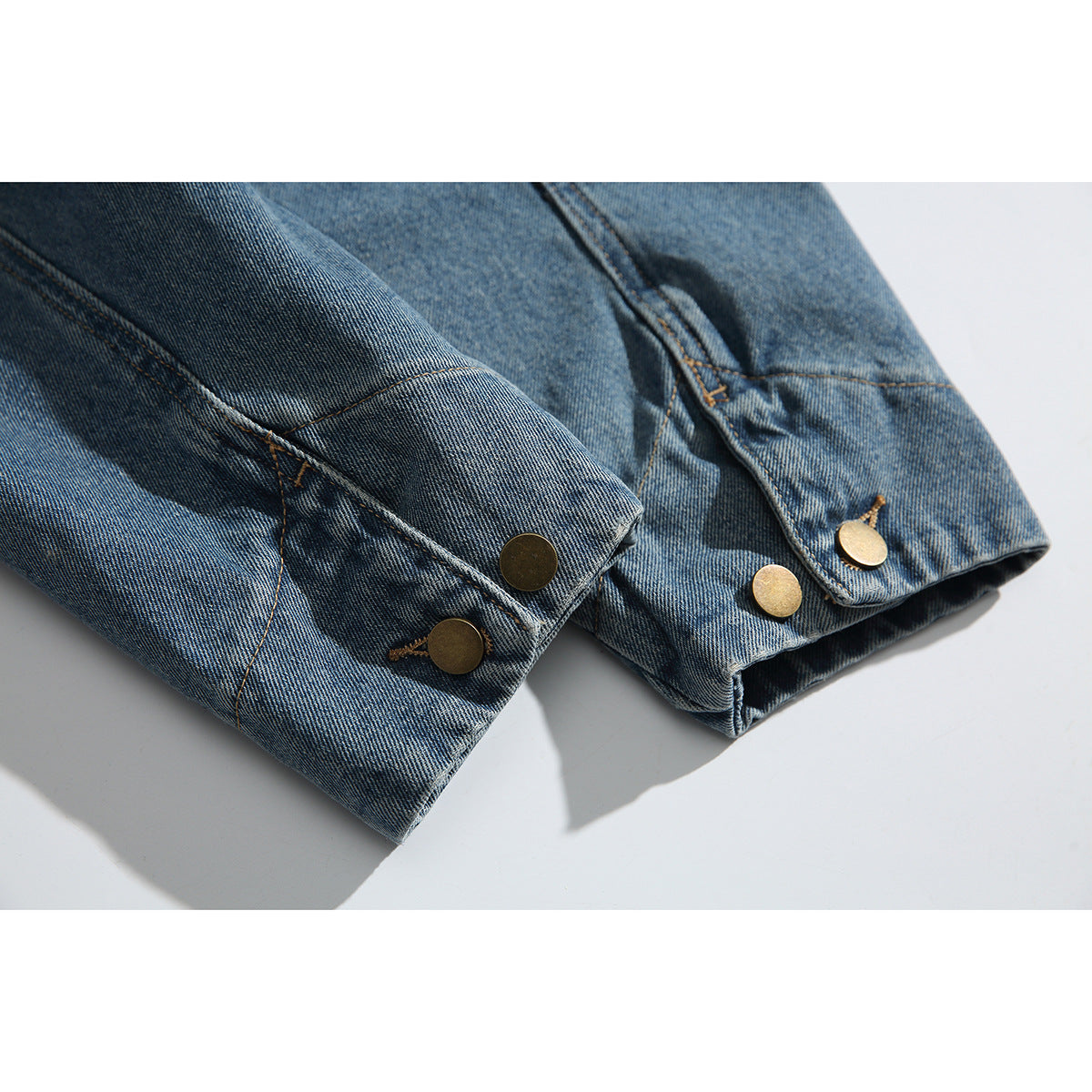 Close-up of blue washed-denim jacket cuffs with round brass-colored buttons and visible stitching.