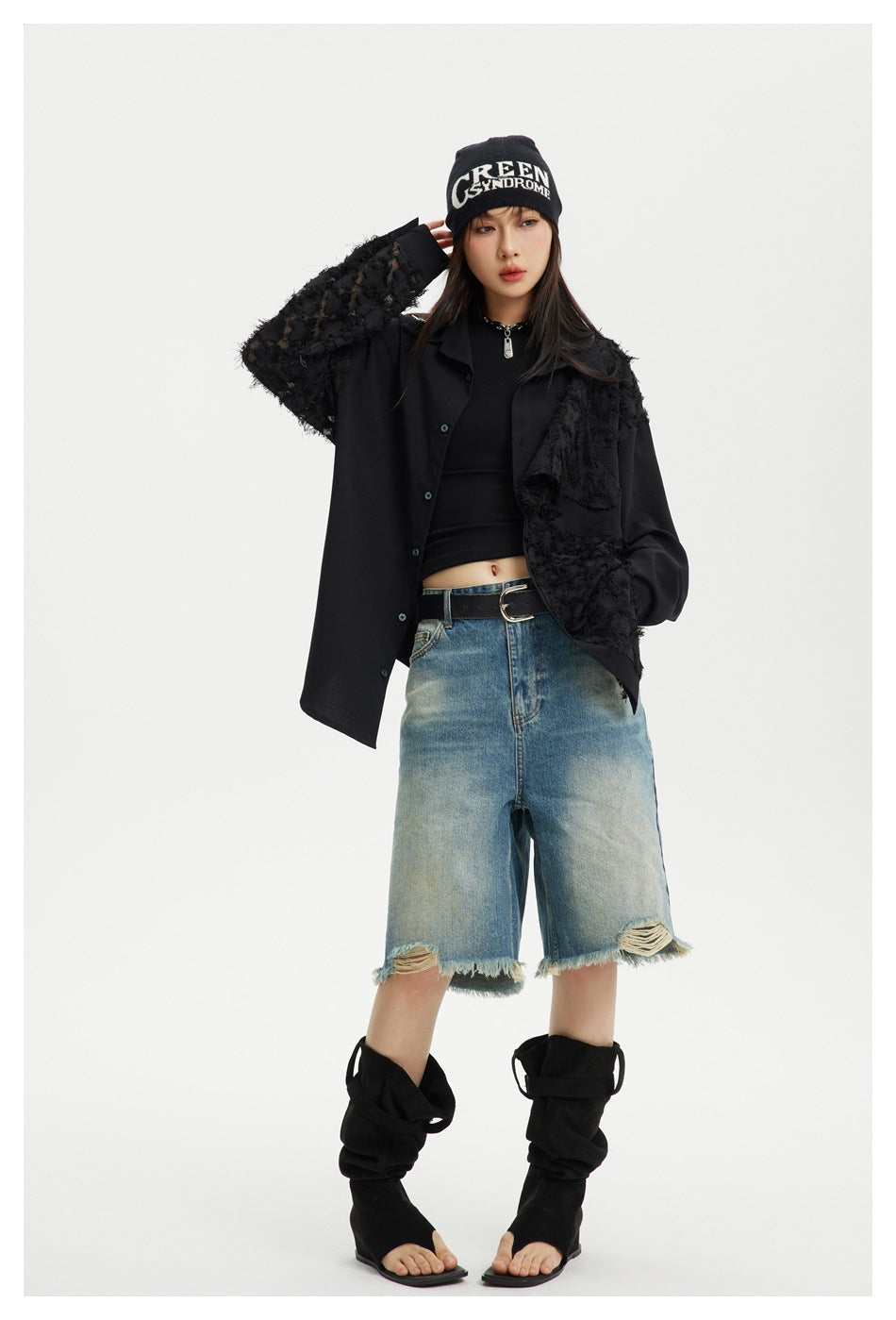 Model with one hand raised wearing the black fringe-panel shirt open over a black top and denim shorts