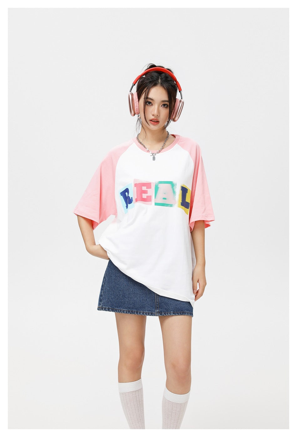 Model wearing a white and pink raglan T-shirt with colorful REAL lettering, shown with a denim skirt.