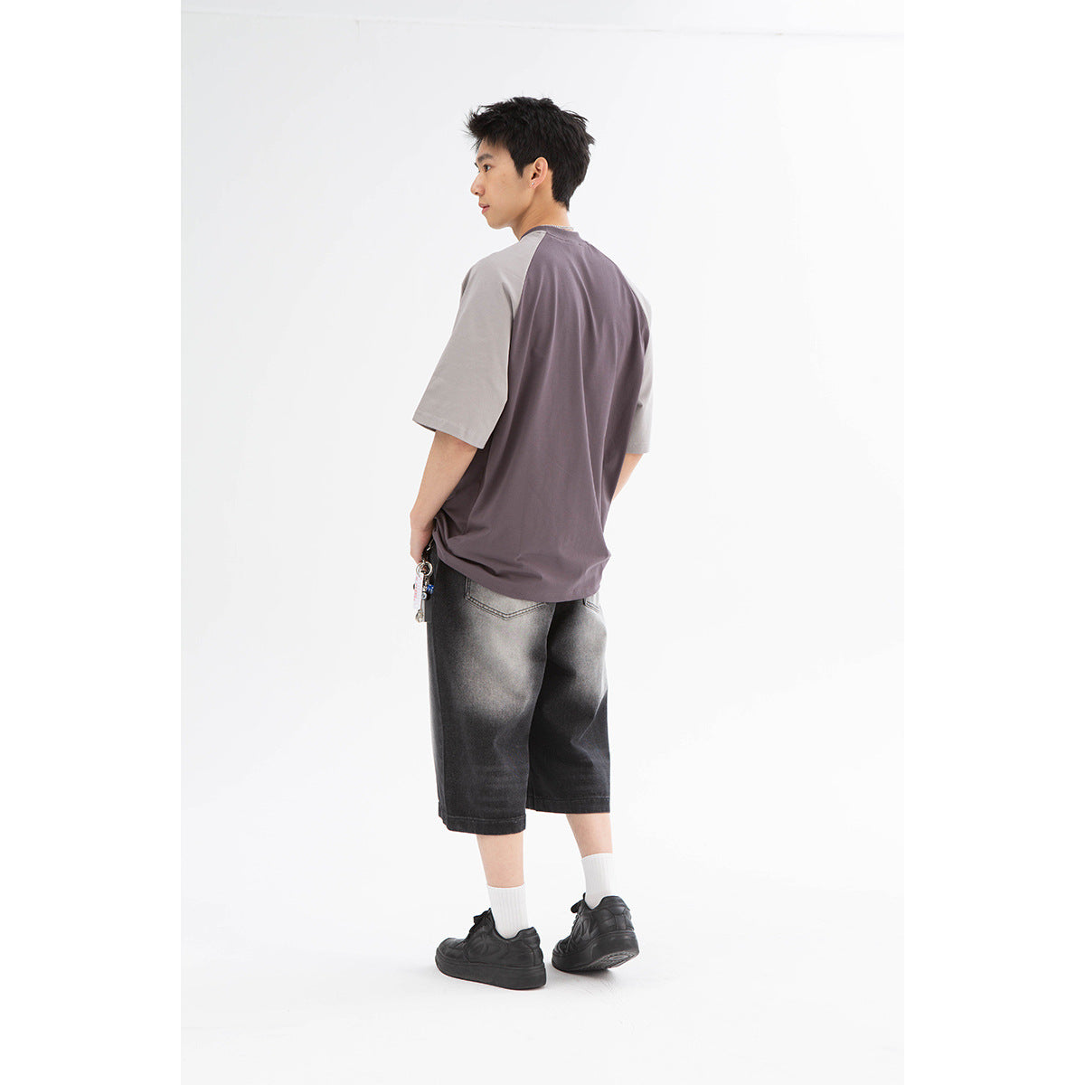 Rear view of a model wearing a charcoal raglan T-shirt with gray sleeves and washed black wide-leg shorts.