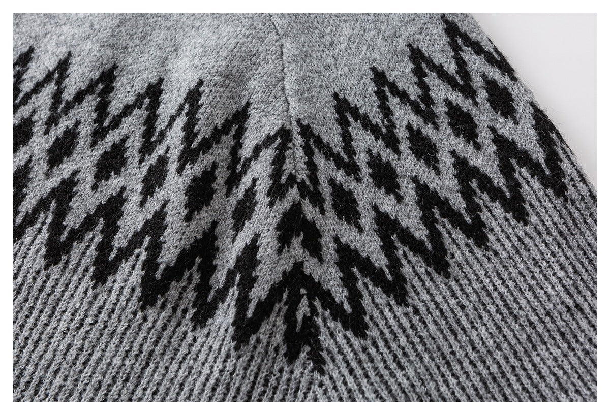 Close-up of a gray knit sweater with a black zigzag pattern and ribbed hem.