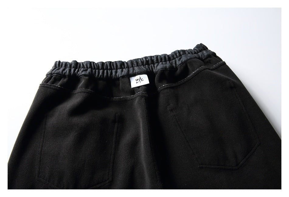 Close-up of black pants showing an elastic waistband, two rear pockets, and a small center label.