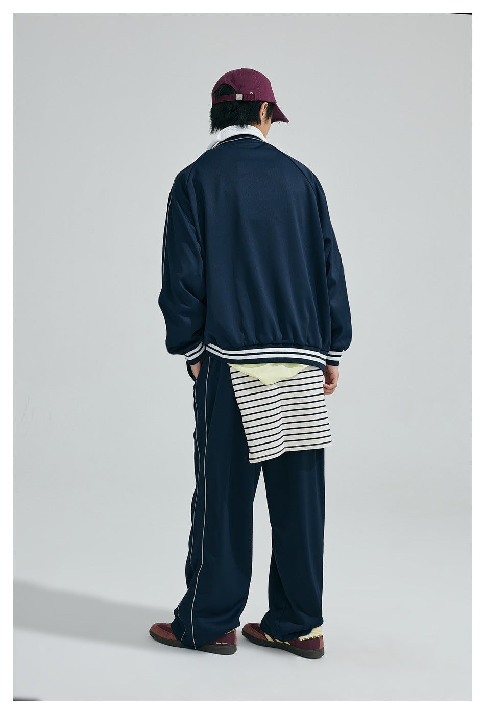 Back view of a model wearing a navy tracksuit with white piping and striped layers at the waist.