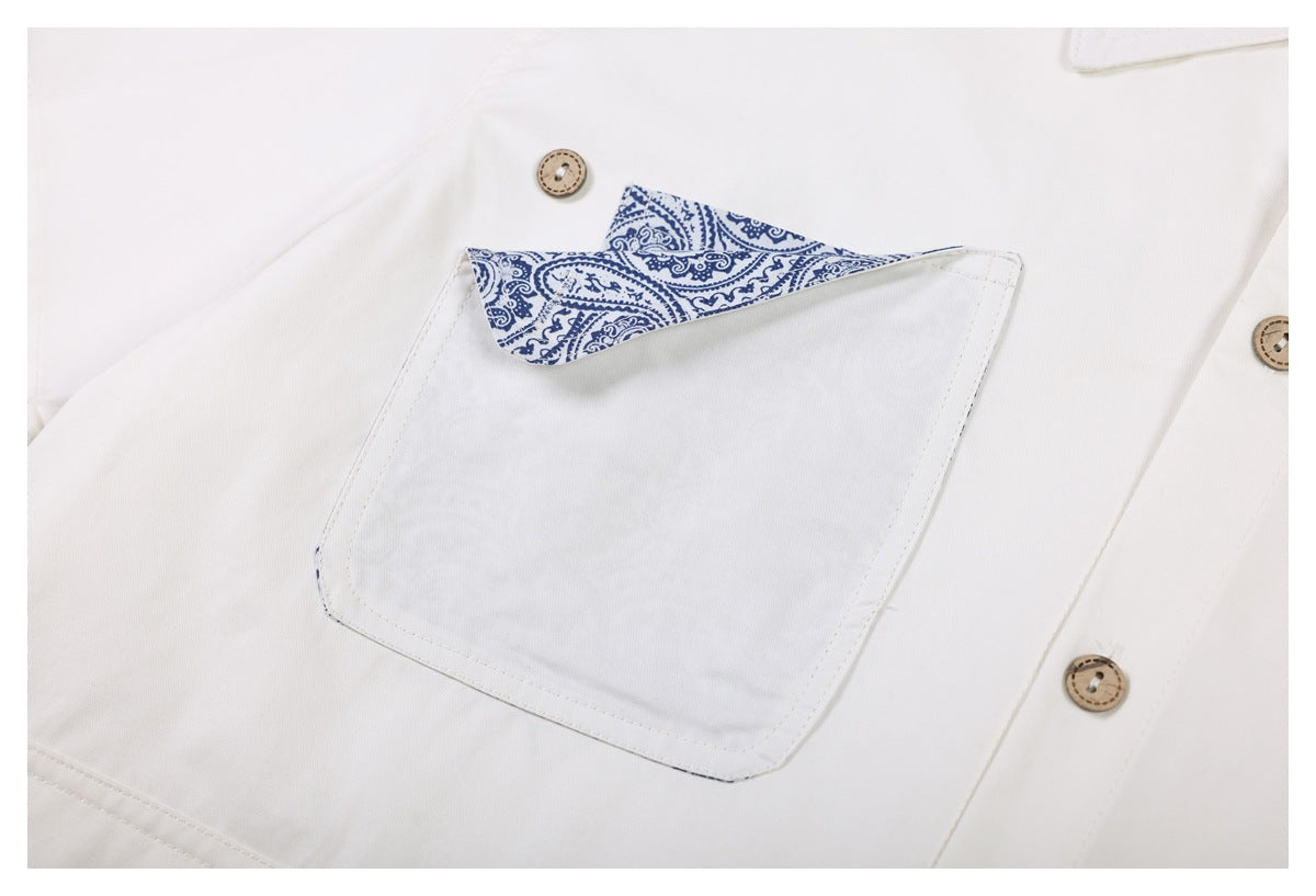 Close-up of an ivory shirt pocket with blue paisley trim and tan buttons.