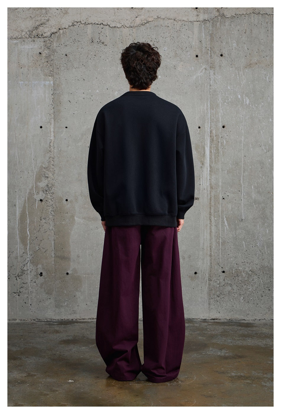 Rear view of a model wearing a plain black crewneck sweatshirt and loose burgundy pants.
