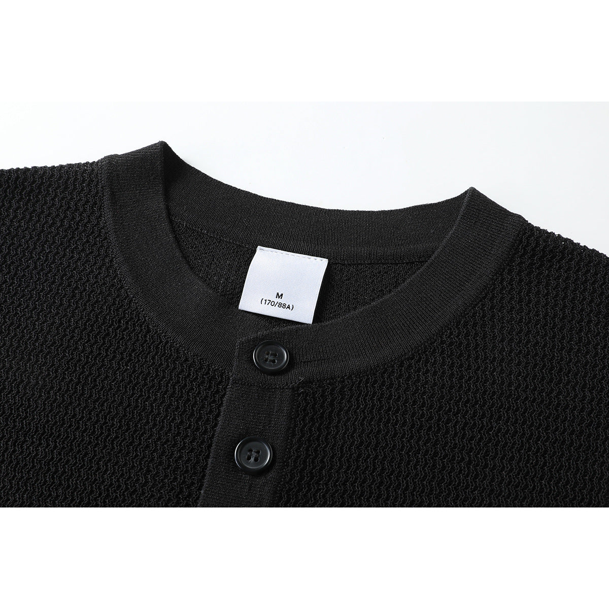 Close-up of a black knit Henley top showing its round neckline, two buttons, and size label.