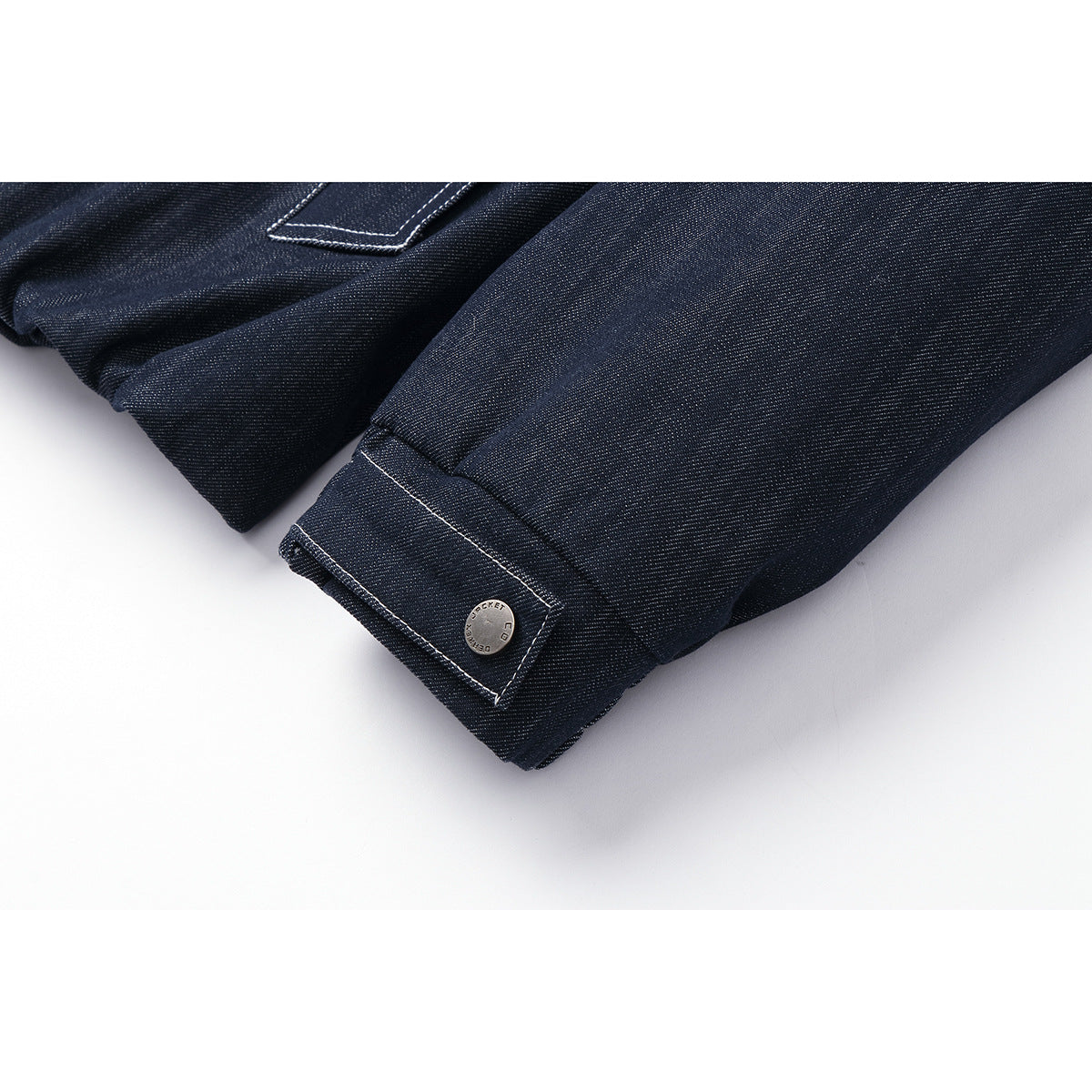 Close-up of a dark indigo jacket sleeve cuff with contrast stitching and a small metal button.
