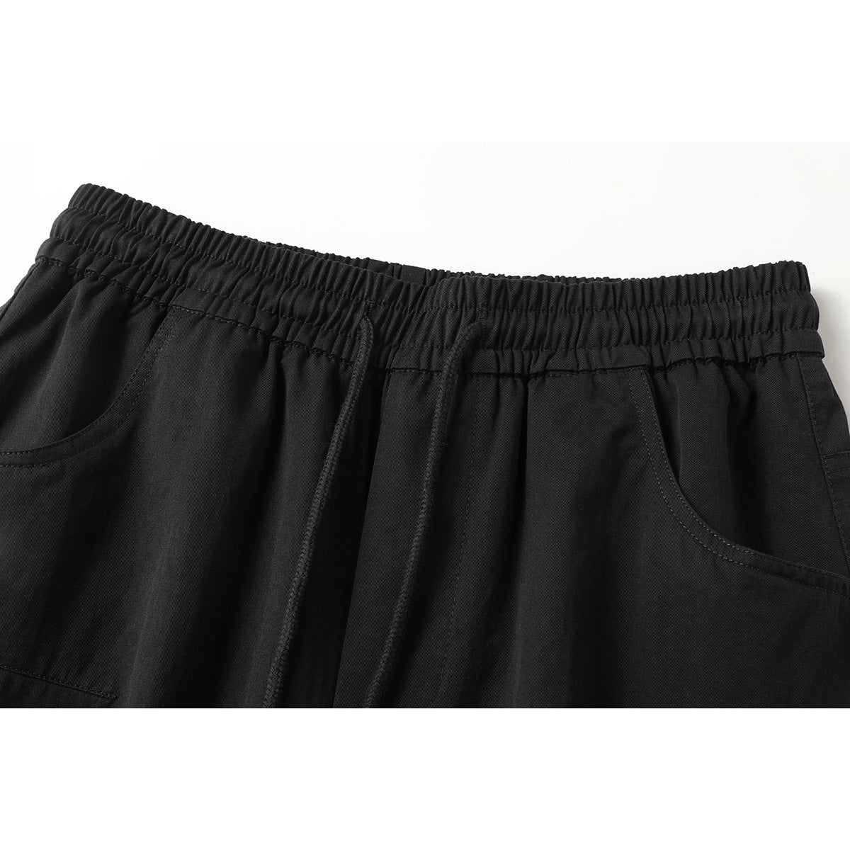 Close-up of black pants showing the elastic drawstring waistband and curved front pockets.
