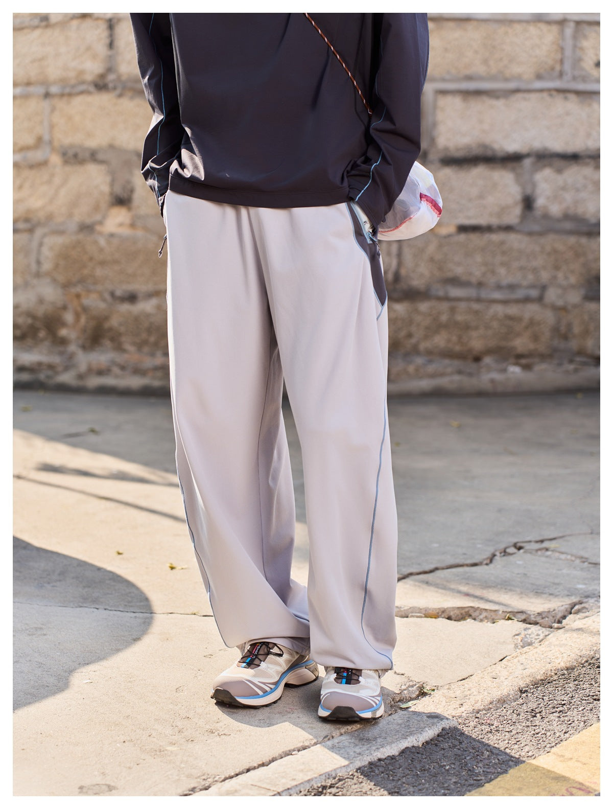 Rear view of loose light-gray trousers with blue piping, worn with a dark top.