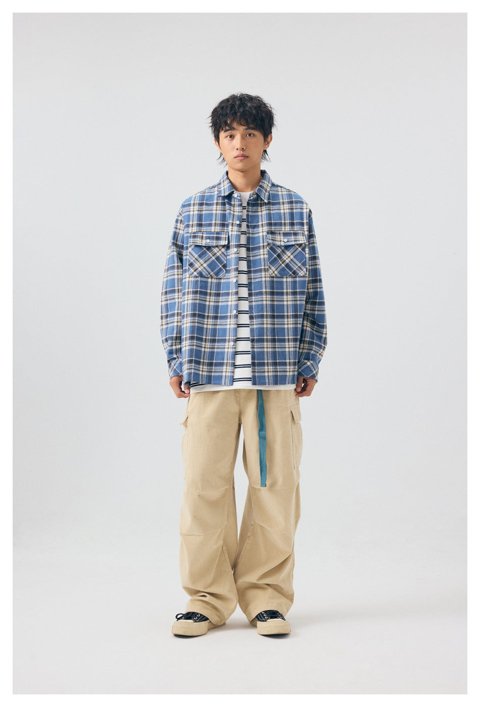 Full-length front view of a model in a blue plaid overshirt, striped tee, and beige cargo pants.