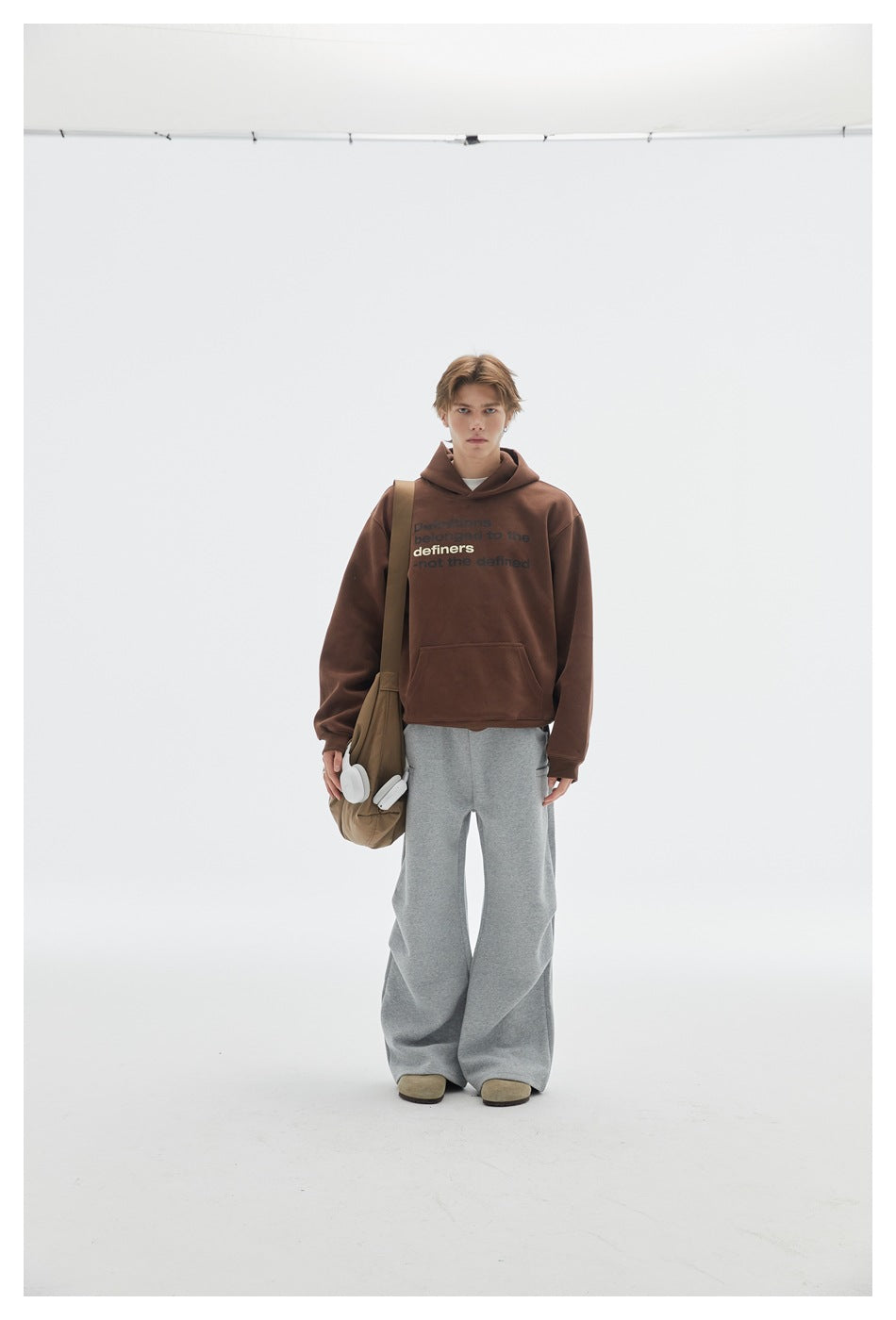 Model wearing heather gray wide-leg sweatpants with a brown hoodie and a tan shoulder bag, front view