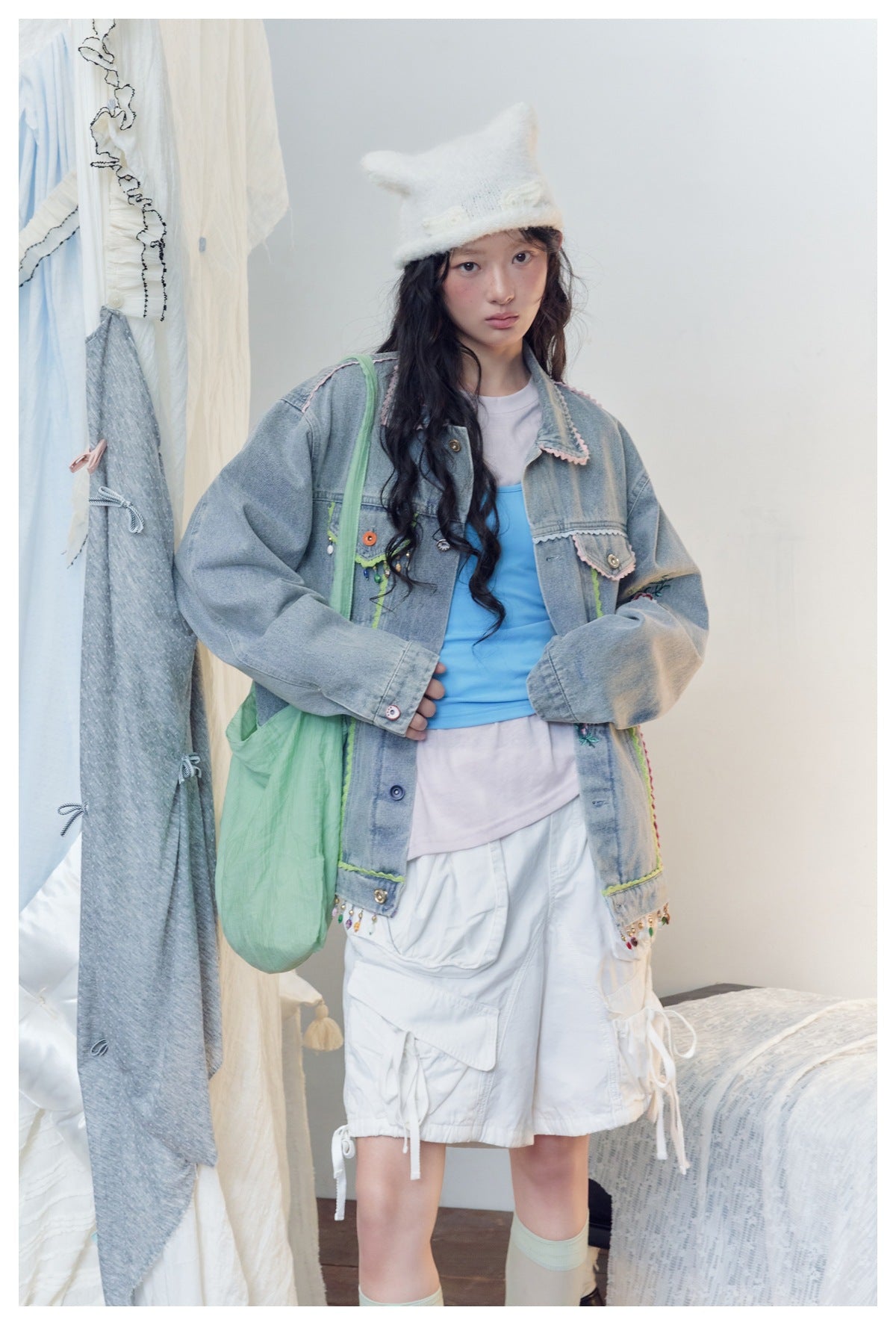 Model wearing an embellished light-blue denim jacket with colorful trim, a blue top and white cargo shorts.