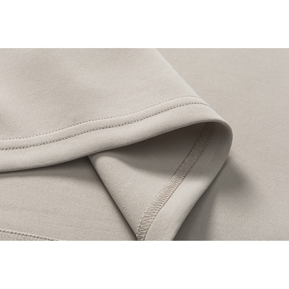 Close-up of the stitched hem and overlocked seam on light beige fabric.