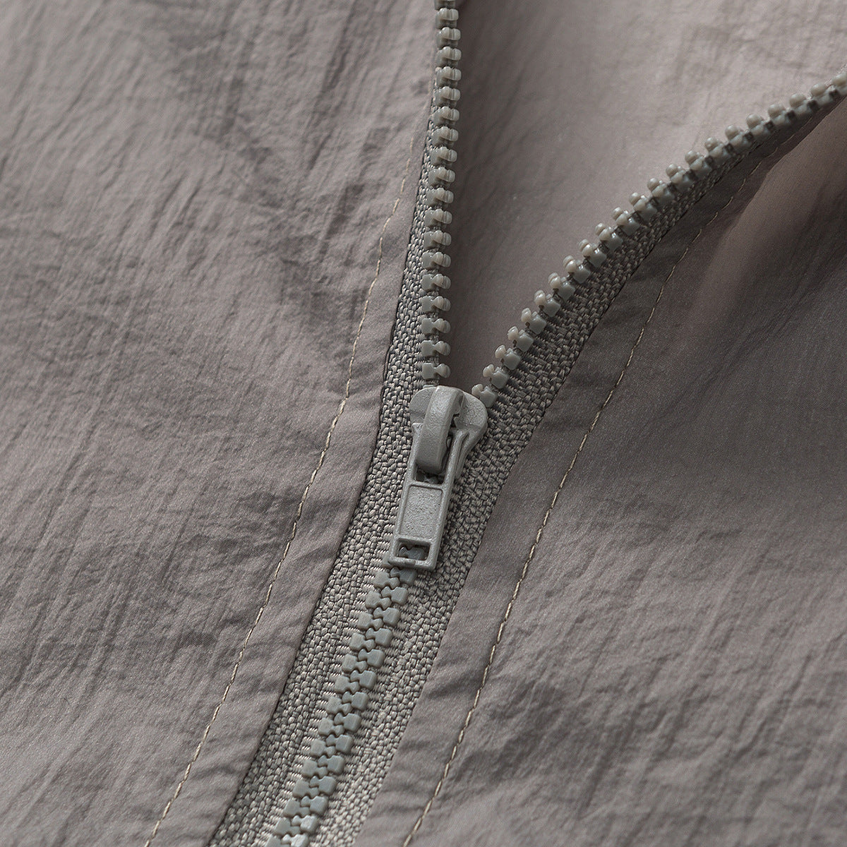 Close-up of a chunky gray zipper and stitching on crinkled taupe-gray fabric.
