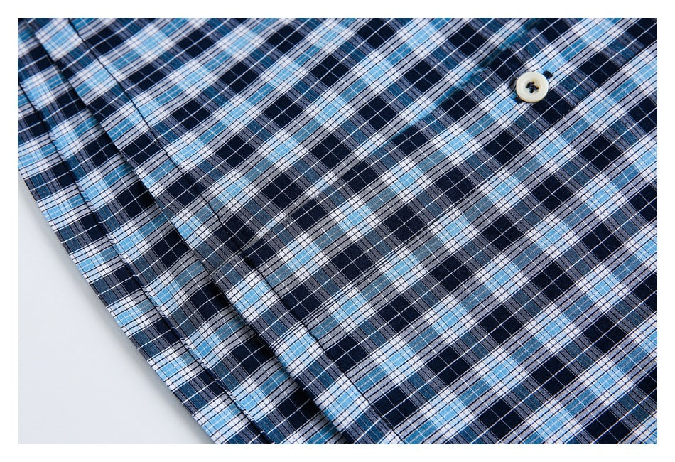 Close-up of a cream button and folded placket on a navy, light blue, and white plaid shirt.