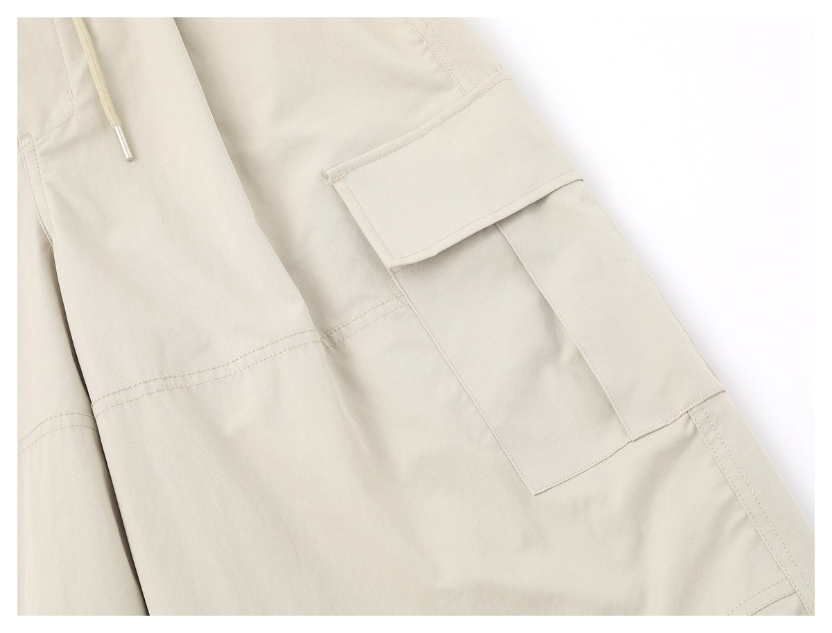 Close-up of a light beige cargo trouser leg with a large flap pocket and stitched panel seams.