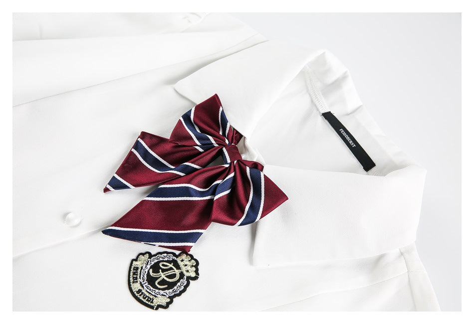 Close-up of a white shirt collar with a burgundy-and-navy striped bow and embroidered crest.
