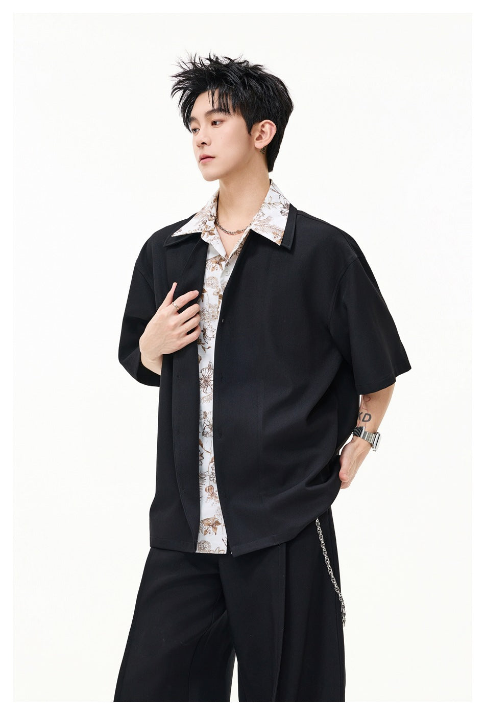 Model wearing an open black short-sleeve shirt over a white top with a brown floral print and collar.
