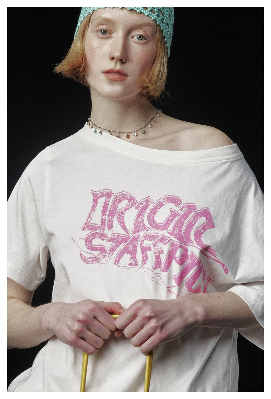 Close-up of an off-white T-shirt with a large distressed pink graphic and a wide, off-shoulder neckline.