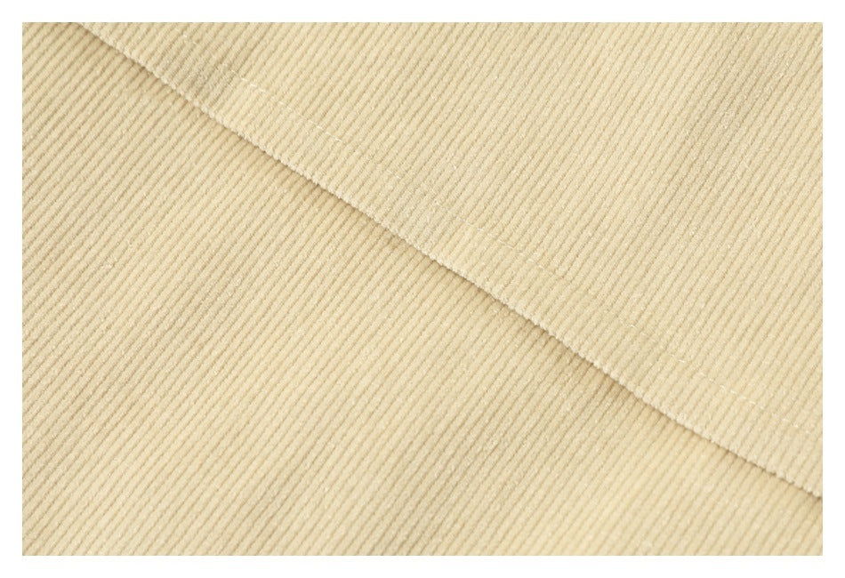 Extreme close-up of the cream jacket's fine corduroy ridges and stitched seam.