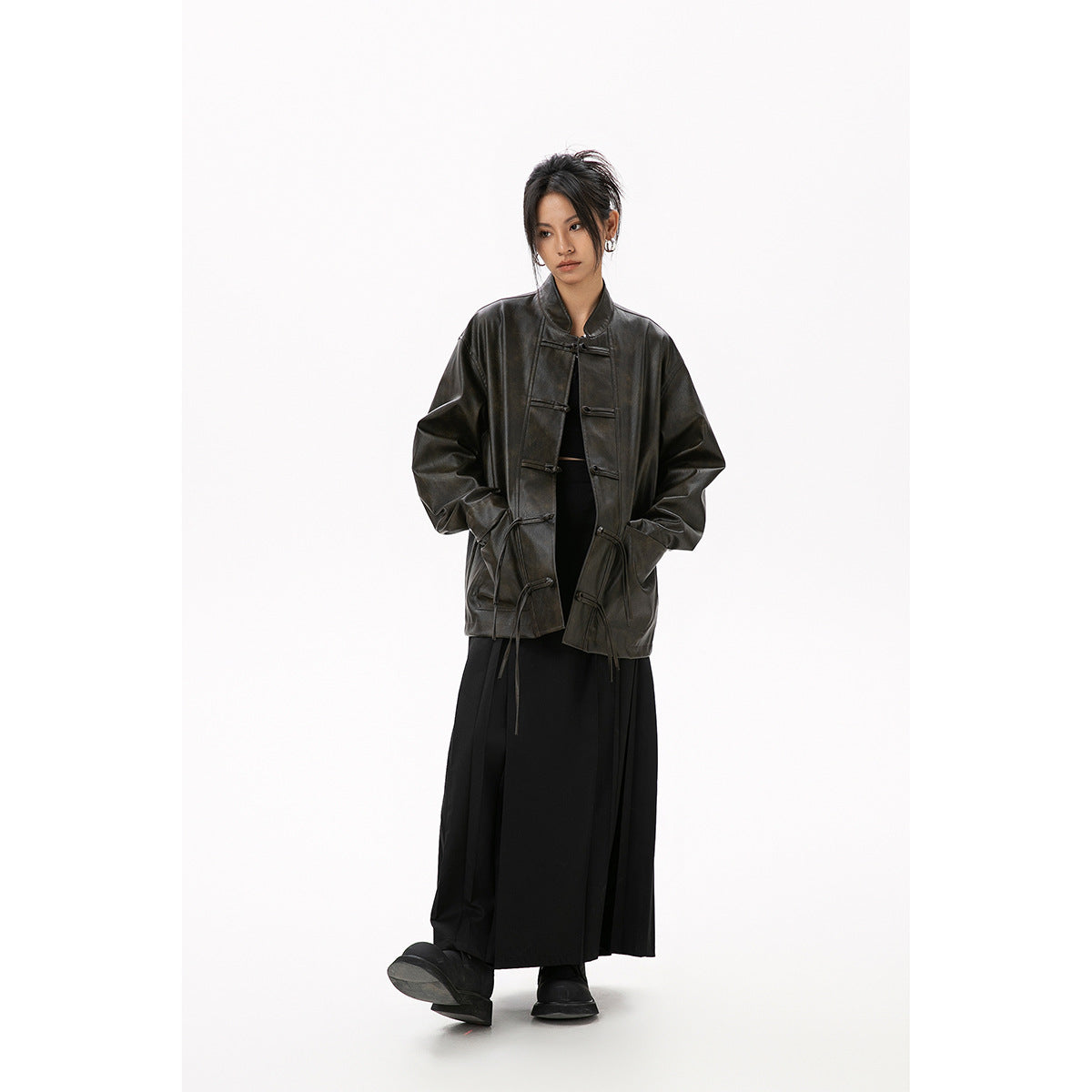 Model wears an oversized dark brown-black jacket with toggle closures over a long black skirt, shown from the front.