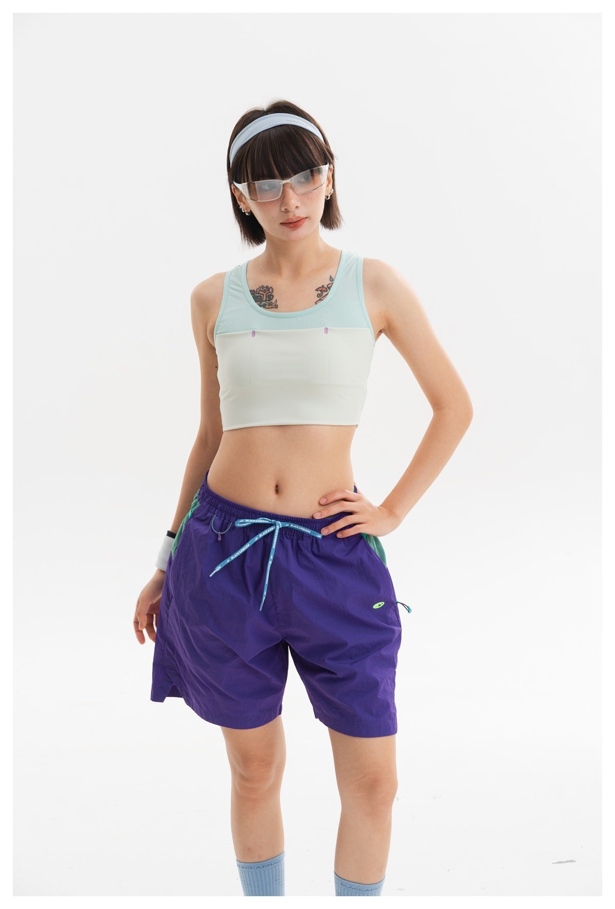 Closer view of a model wearing a mint and ivory cropped tank with purple drawstring shorts.