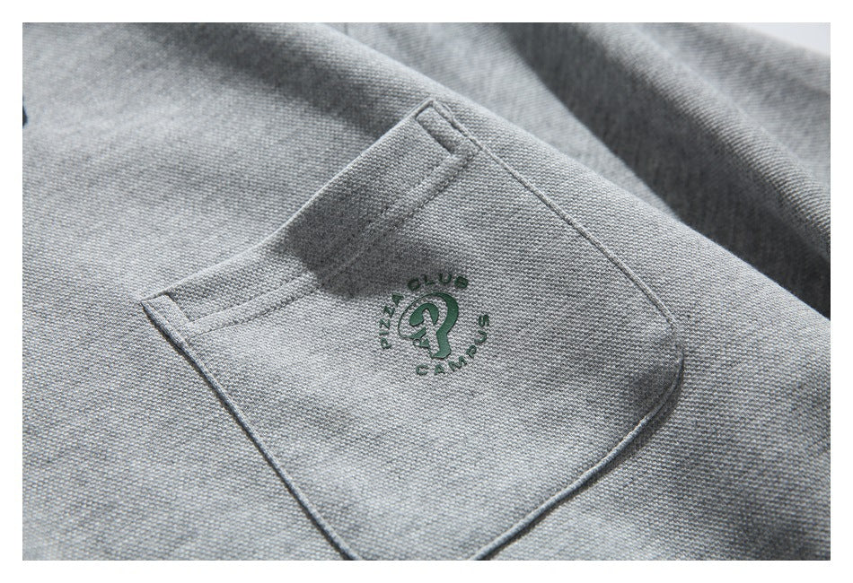 Close-up of a gray sweatshirt pocket with a small dark green embroidered emblem and lettering.
