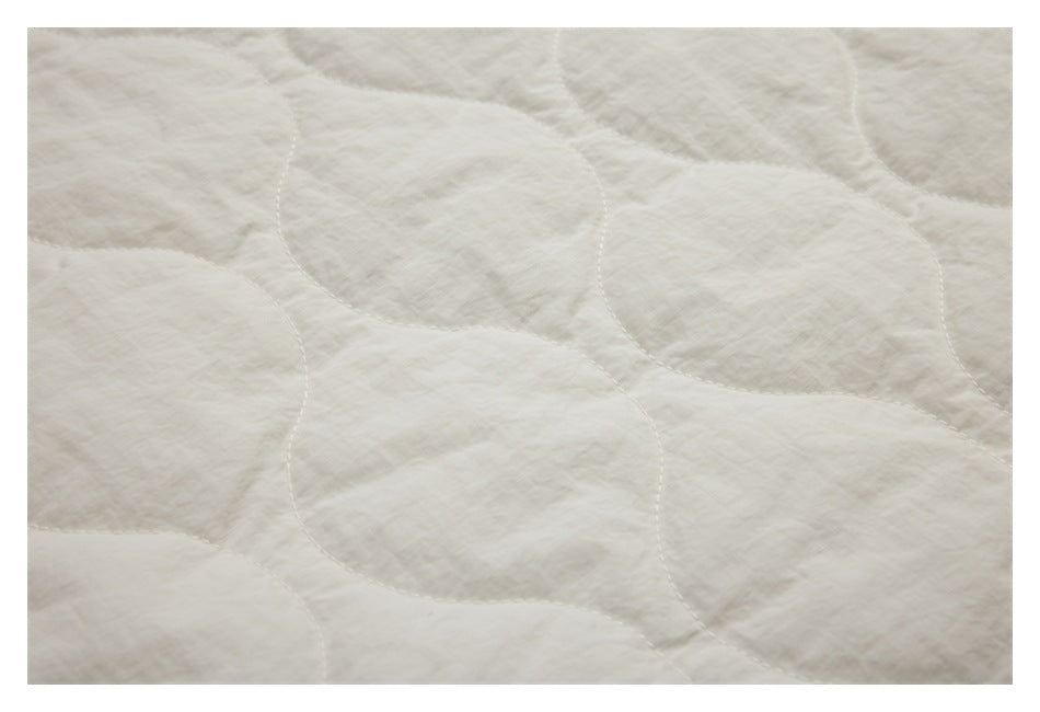 Close-up showing the ivory jacket's soft, irregular wave-pattern quilting and stitching.