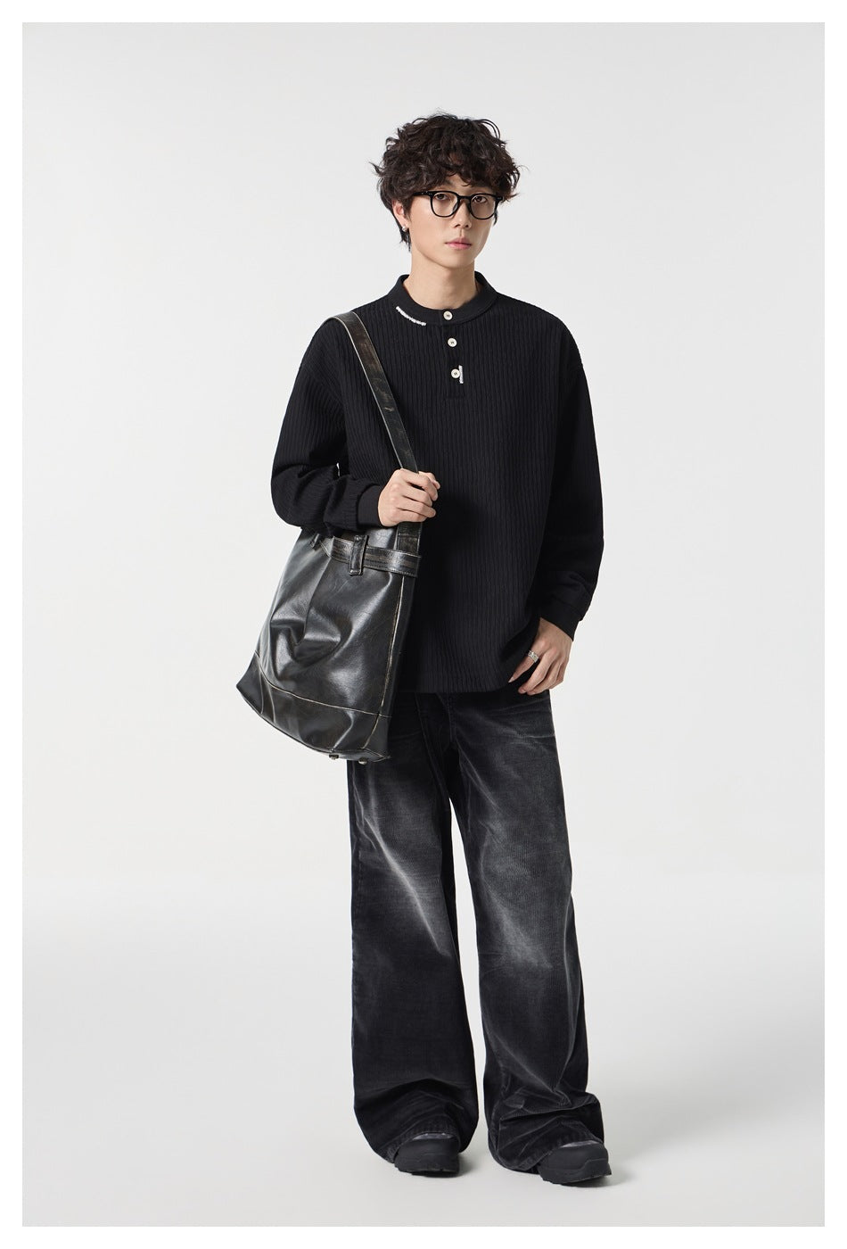 Person wearing a black ribbed Henley top with wide dark pants and a black leather shoulder bag, full-length view