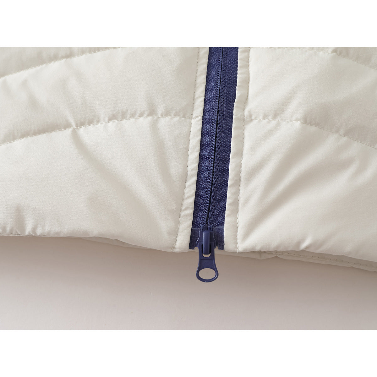 Close-up of the dark blue zipper and pull at the hem of an ivory quilted jacket.