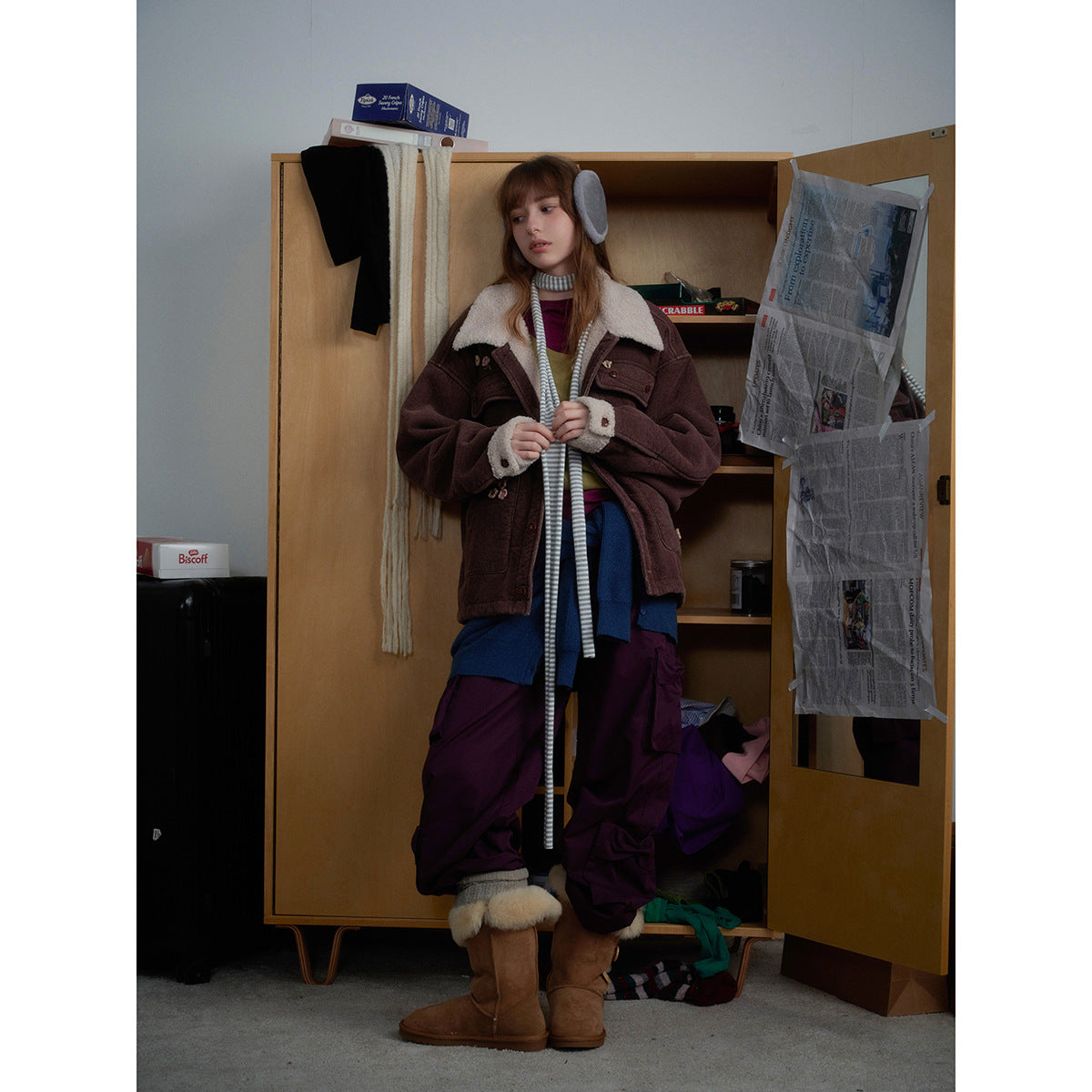 Model wearing an oversized brown jacket with a cream shearling-style collar and cuffs, layered over colorful clothes.