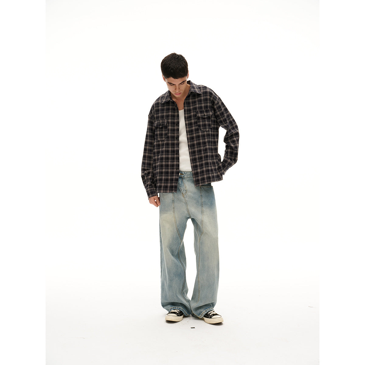 Model wearing an open charcoal plaid button-up shirt with two chest pockets, a white tee, and loose light-wash jeans.
