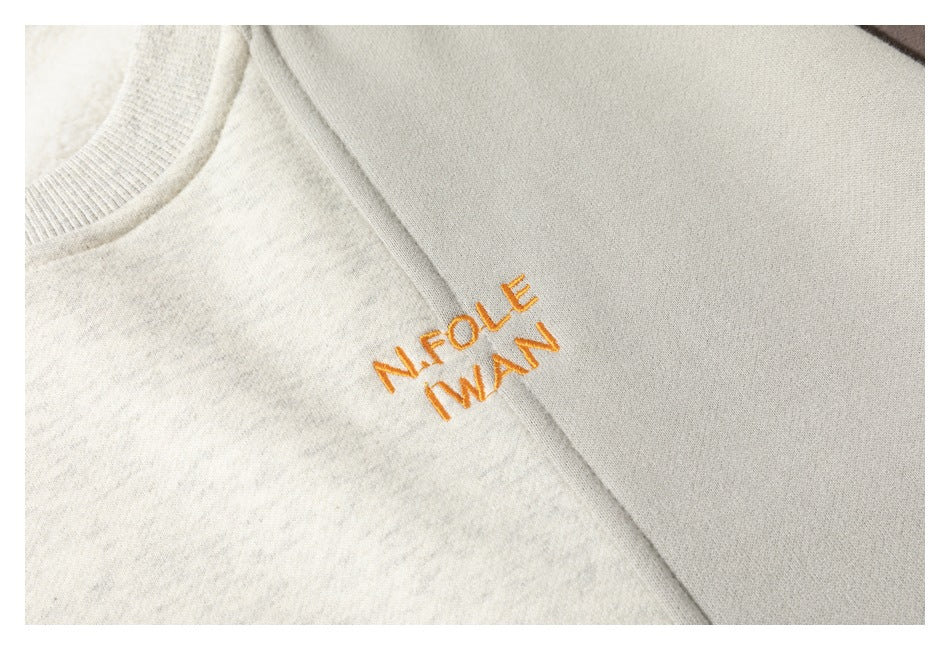 Close-up of orange embroidered lettering on a cream color-block sweatshirt.