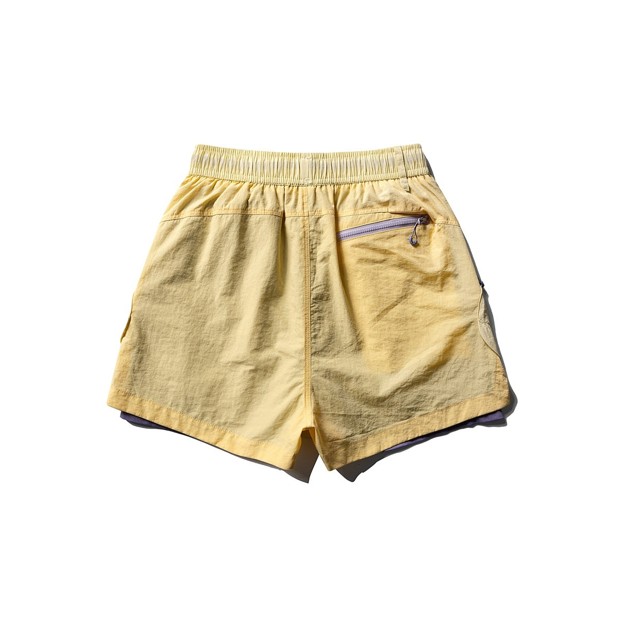 Back view of yellow athletic shorts with an elastic waistband, angled zip pocket, and purple lining at the hem.