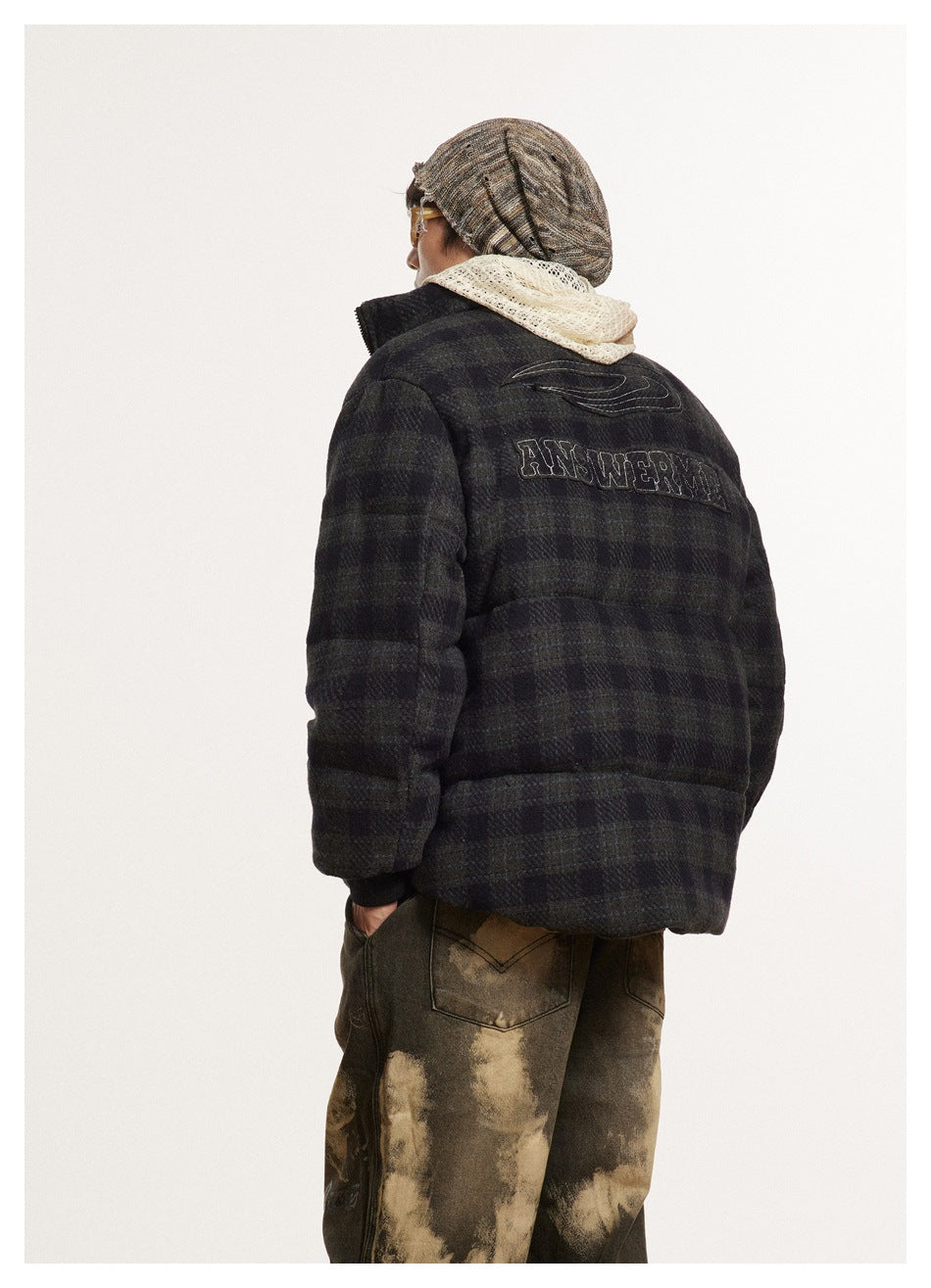Close rear view of a dark plaid puffer jacket with outlined back lettering and a cream hood visible above the collar.