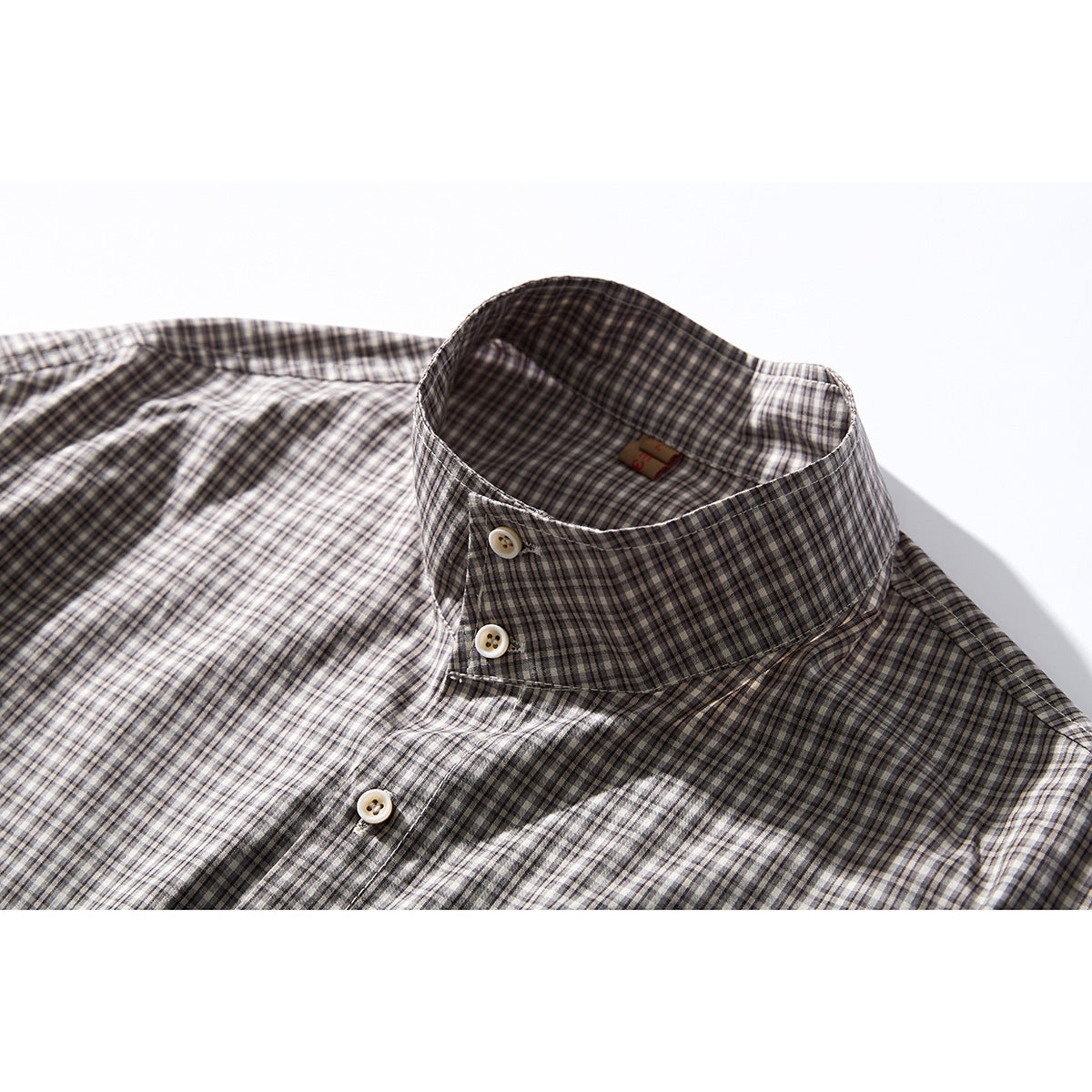 Close-up of a gray, black, and cream checked shirt collar with cream buttons.