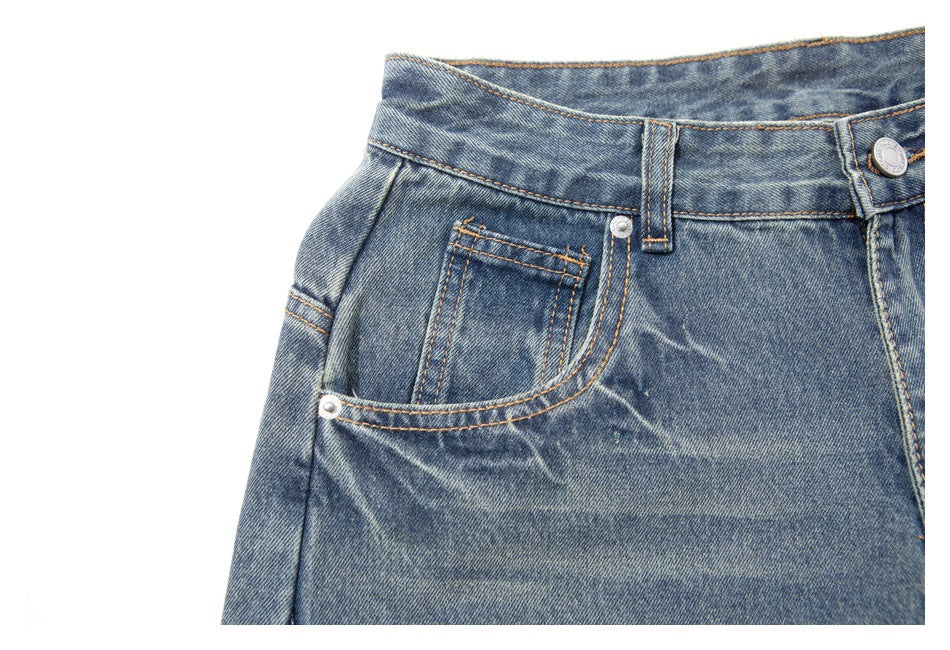 Close-up of blue jeans showing the waistband, button, belt loop, and front pocket with orange stitching.